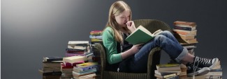 Niña sentada sobre un sillon con libros alrededor, ella se encuentra leyendo